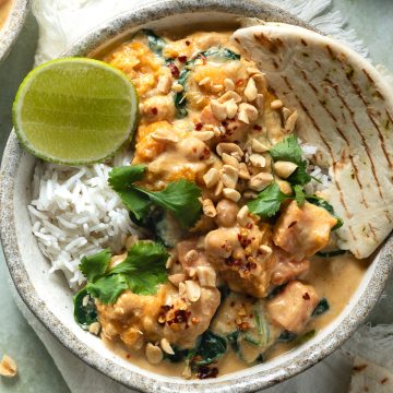 A bowl of chickpea and pumpkin curry served with rice, naan and fresh lime.