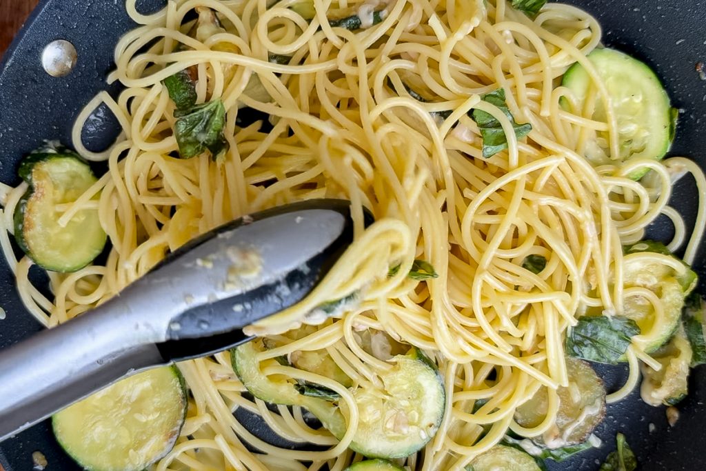 Spaghetti being tossed together with the courgettes, cheese and basil.