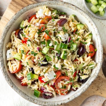Greek orzo salad in a bowl on a wooden board.