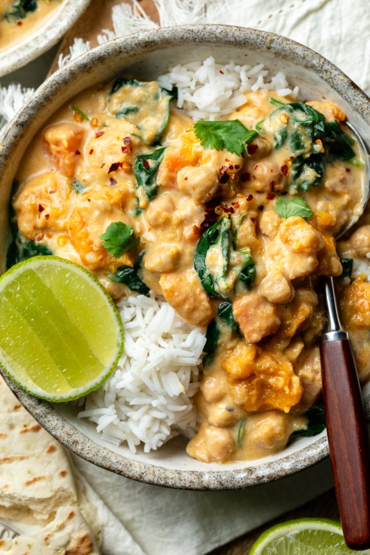 Close up of a bowl of pumpkin and chickpea curry with rice and lime.
