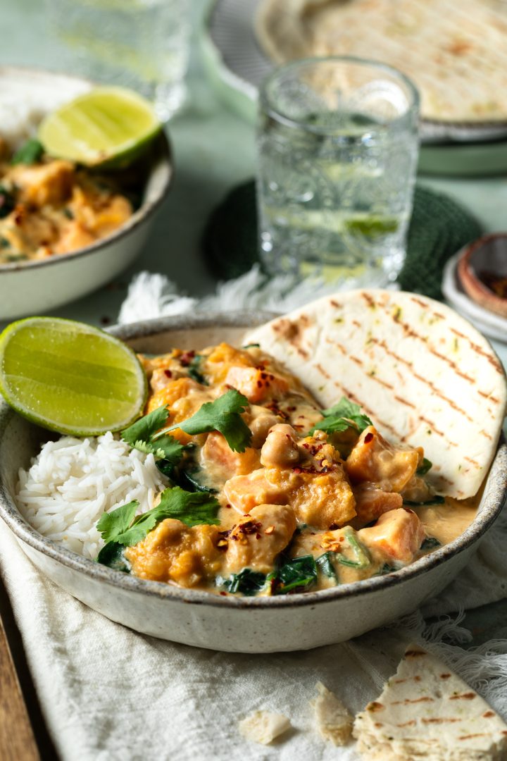 Side view of a bowl of pumpkin curry served with naan and water glasses just visible.