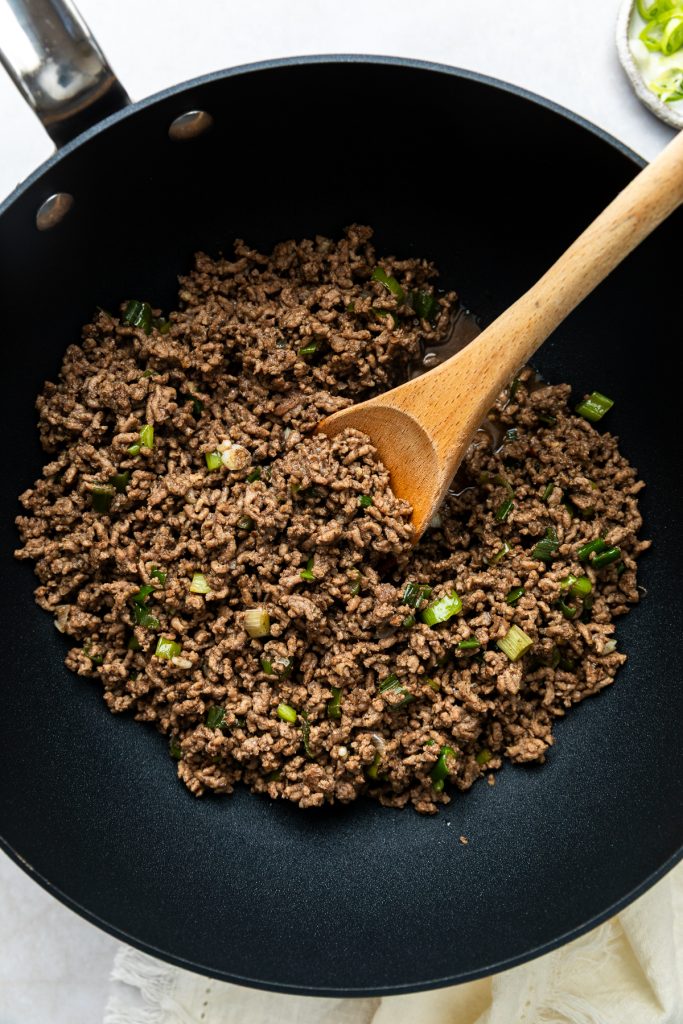 The stir fried beef mince in the pan with a wooden spoon.