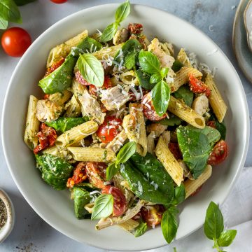 A bowl of chicken pesto pasta, with extra parmesan cheese in the top right corner.
