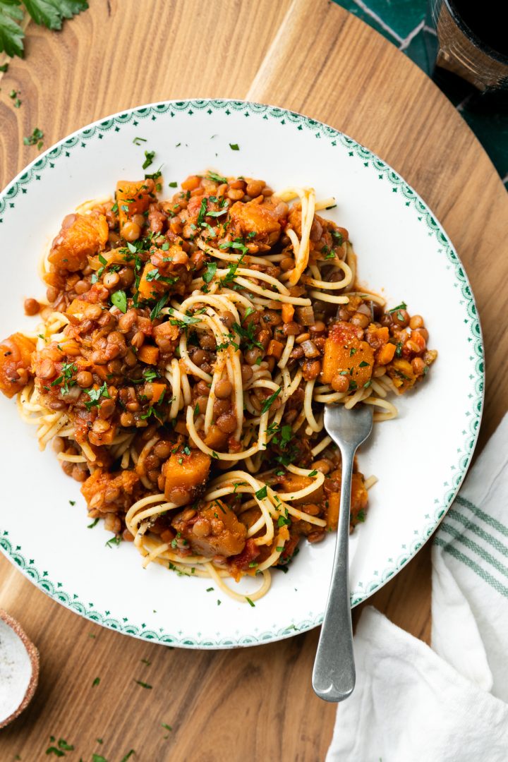 A plate of lentil ragu with pasta, with a fork positioned to hold some pasta.