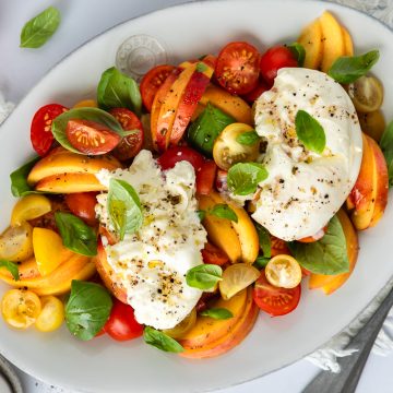 An oval serving plate of burrata and peach salad.