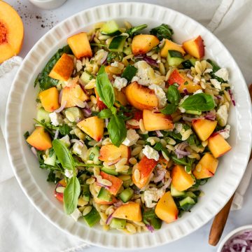 A white bowl of orzo salad with peaches, feta and rocket.
