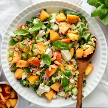 A bowl of peach and orzo salad with a wooden spoon.