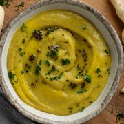 A bowl of spiced parsnip soup topped with cooked spices and served with naan bread on the side.