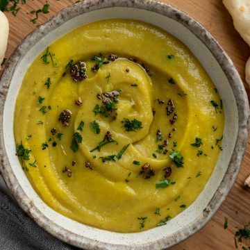 A bowl of spiced parsnip soup topped with cooked spices and served with naan bread on the side.