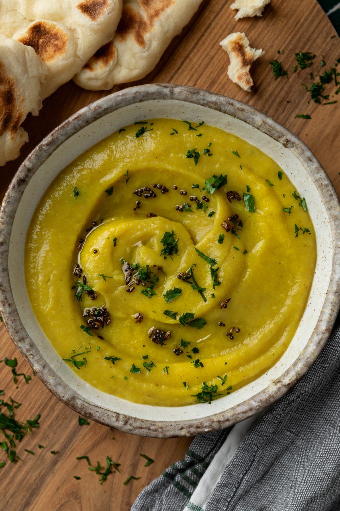 The parsnip soup in a bowl topped with fresh herbs and spices.