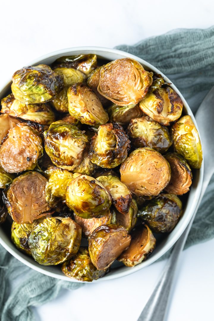 The roasted Brussels sprouts in a bowl with a serving spoon to the right side.