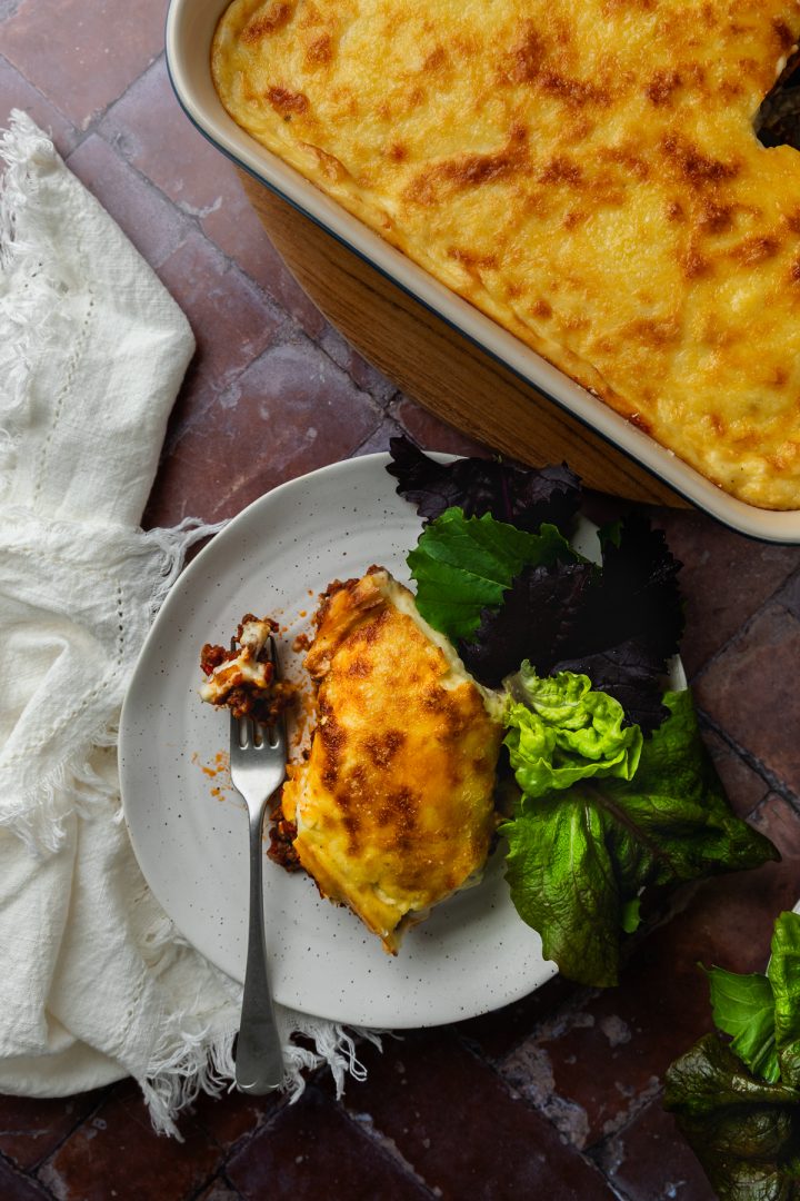 A portion of the Greek lasagna on a plate served with a green salad.