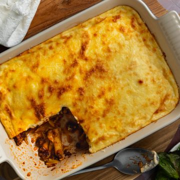 A dish of pastitsio with a portion taken out to show the beef and pasta layers.