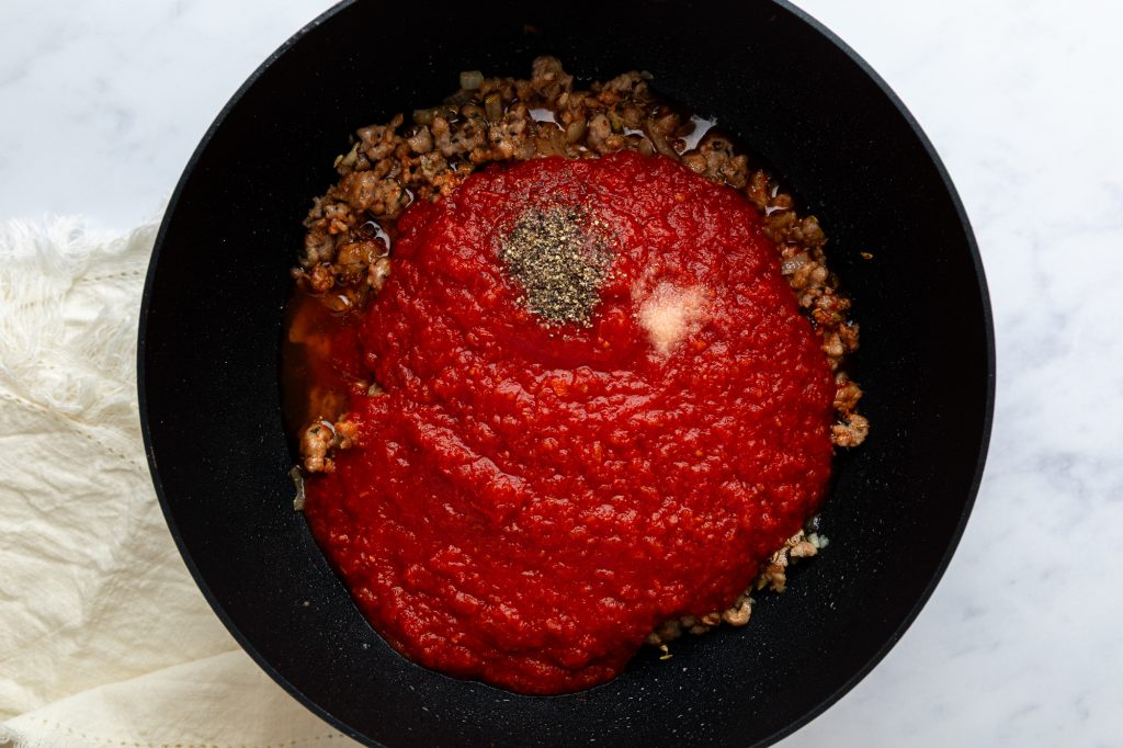The sauce ingredients, including tomatoes, added to the browned sausagemeat.