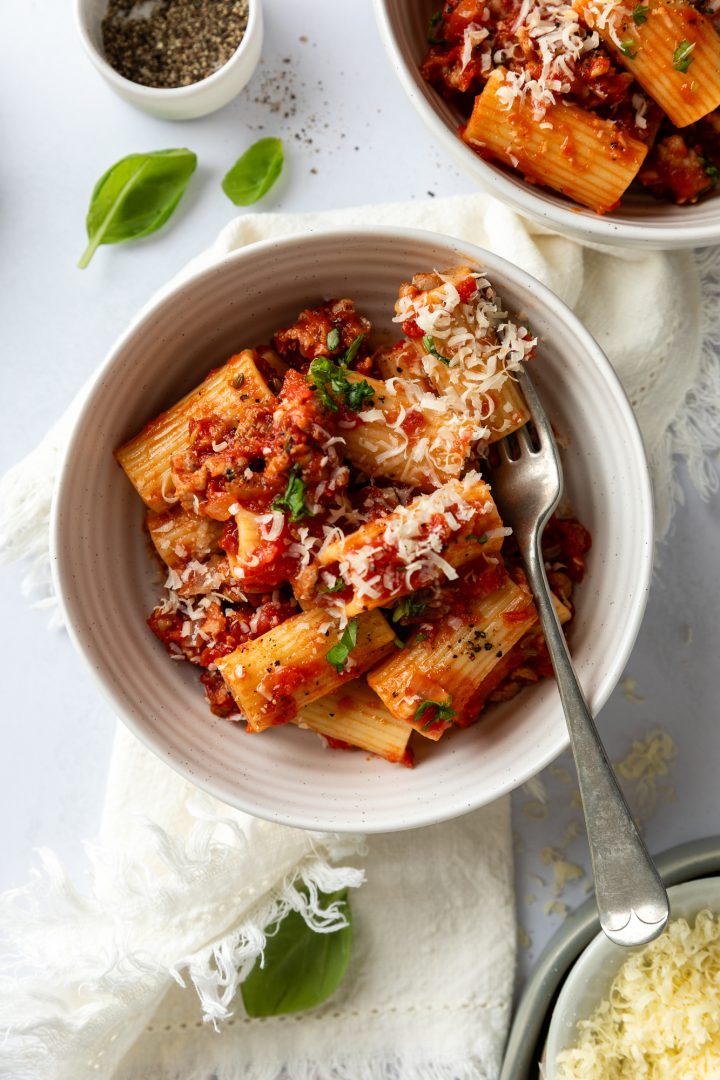 A serving of sausage and fennel pasta in a bowl with a fork ready to eat.