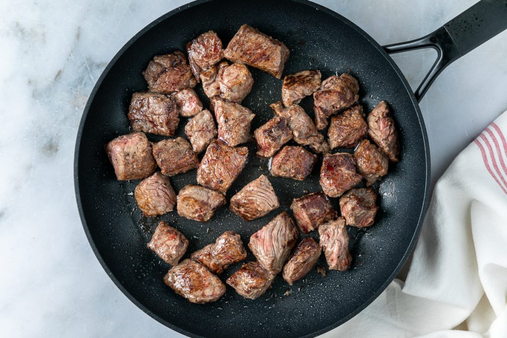 The browned beef in a frying pan.