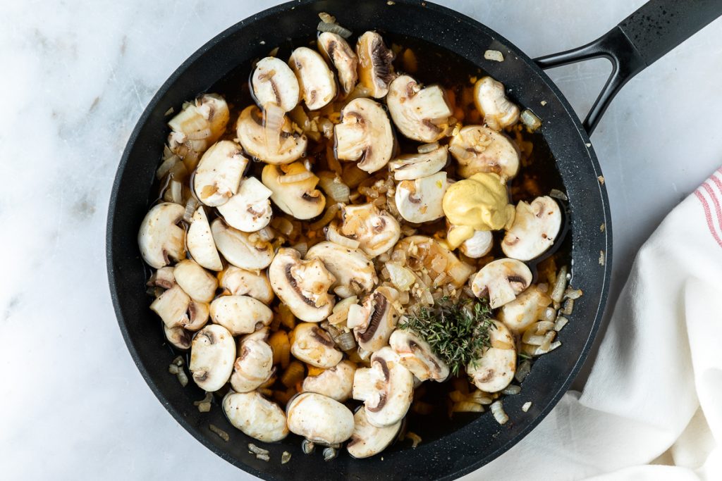 Sliced mushrooms, thyme and mustard added to the frying pan.