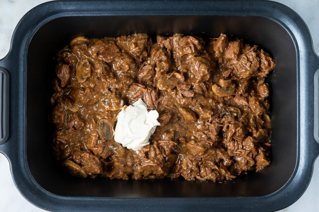 The cooked beef in the slow cooker with a spoonful of sour cream added.