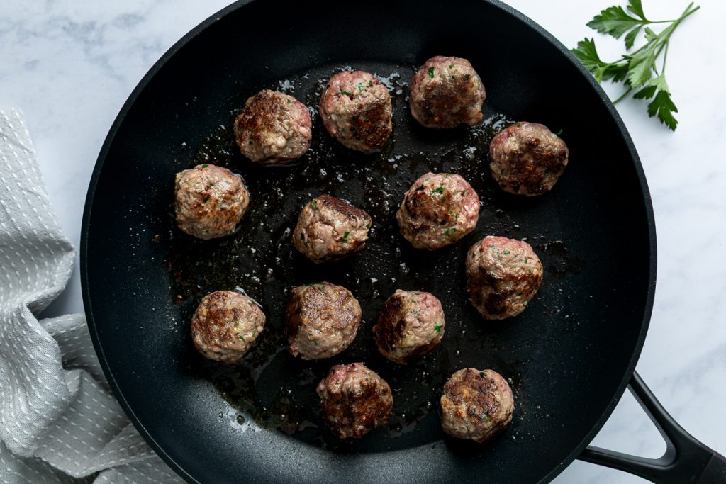 The browned meatballs in a frying pan.