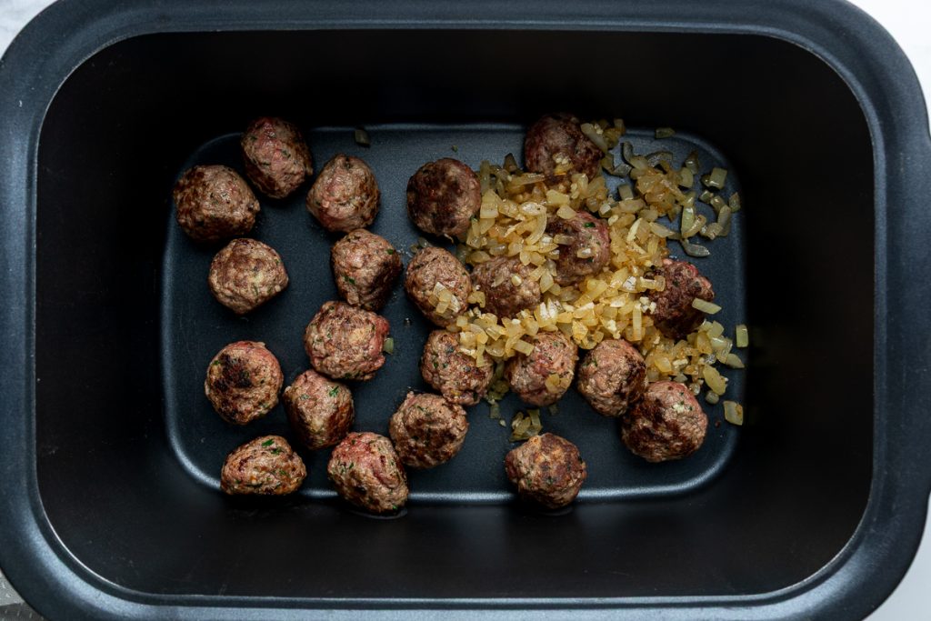 The cooked meatballs and onion in the slow cooker.