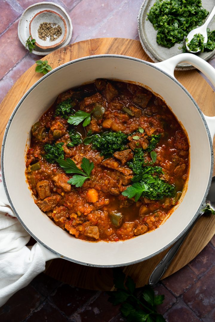 A pan of cooked beef stew topped with chimichurri and fresh parsley.