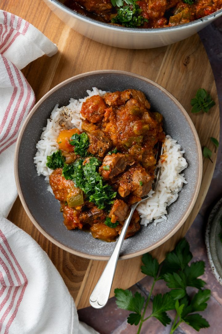 A bowl of beef stew served on rice, topped with chimichurri sauce.