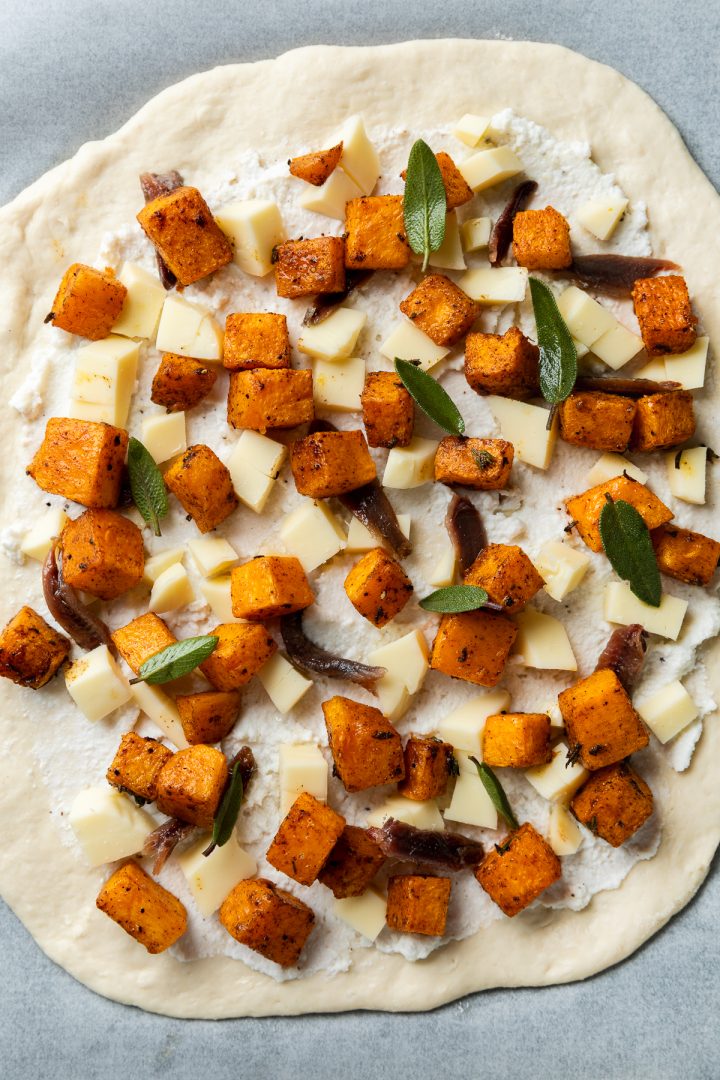 Raw pizza dough topped with roasted butternut squash, anchovies and sage leaves.