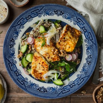 Quinoa salad topped with pan fried halloumi and served on a blue plate.
