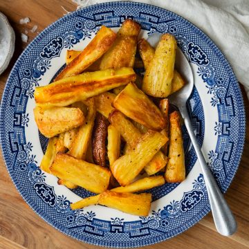 Roast parsnips on a blue serving plate with a spoon ready to serve.