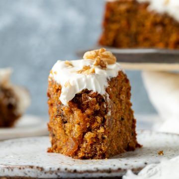 A slice of carrot cake on a plate with a bite taken out to show how moist the cake it.
