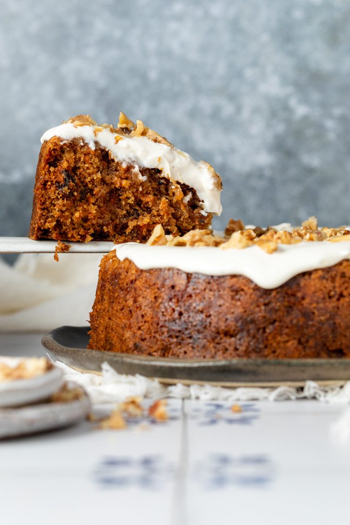 A cake slice holding up a side view of a slice of carrot cake.