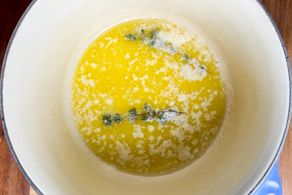 The melted butter in a pan with thyme and garlic.