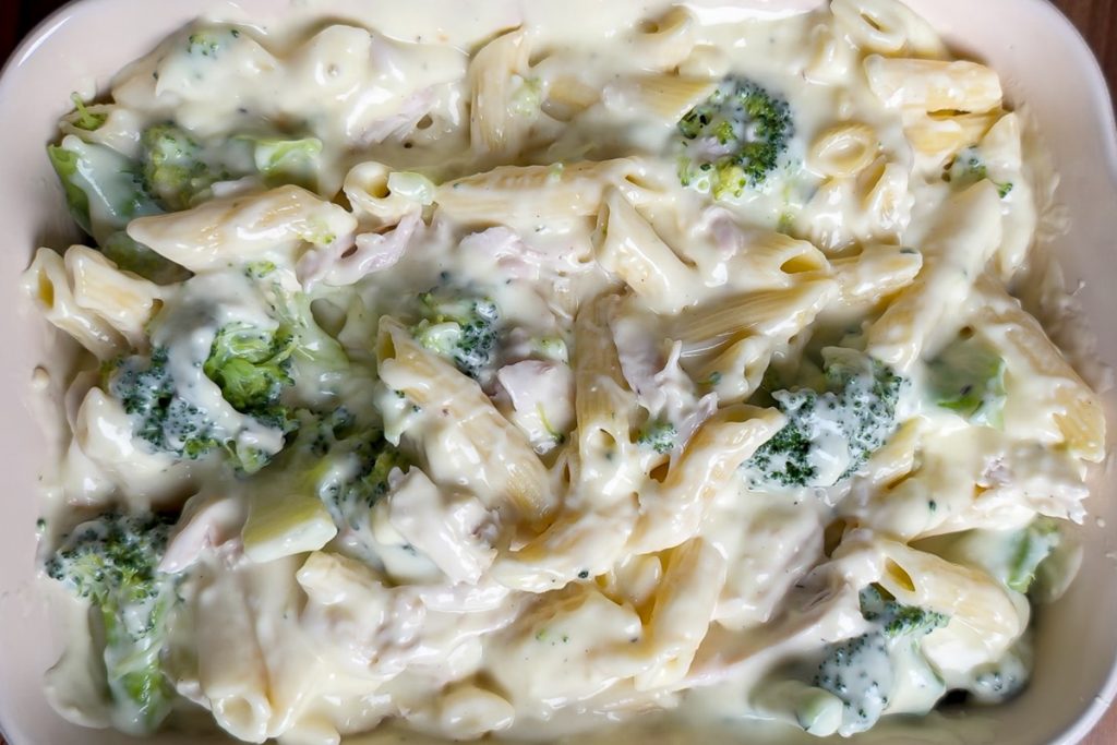 The creamy chicken sauce mixed with broccoli and pasta in the baking dish ready for the oven.