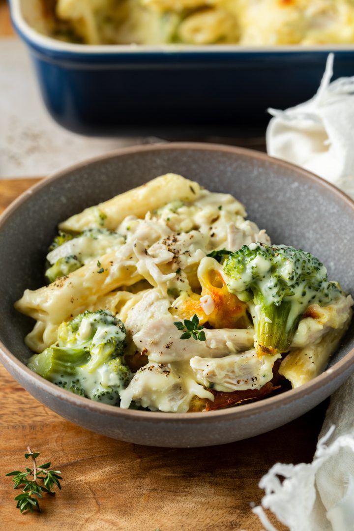 A bowl of chicken broccoli pasta, with the rest of the bake just visible behind.