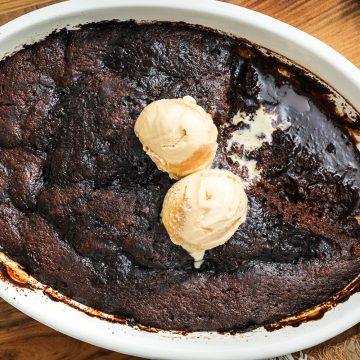 Self saucing chocolate pudding topped with two scoops of ice cream, and a section taken out to show the thick chocolate sauce underneath.