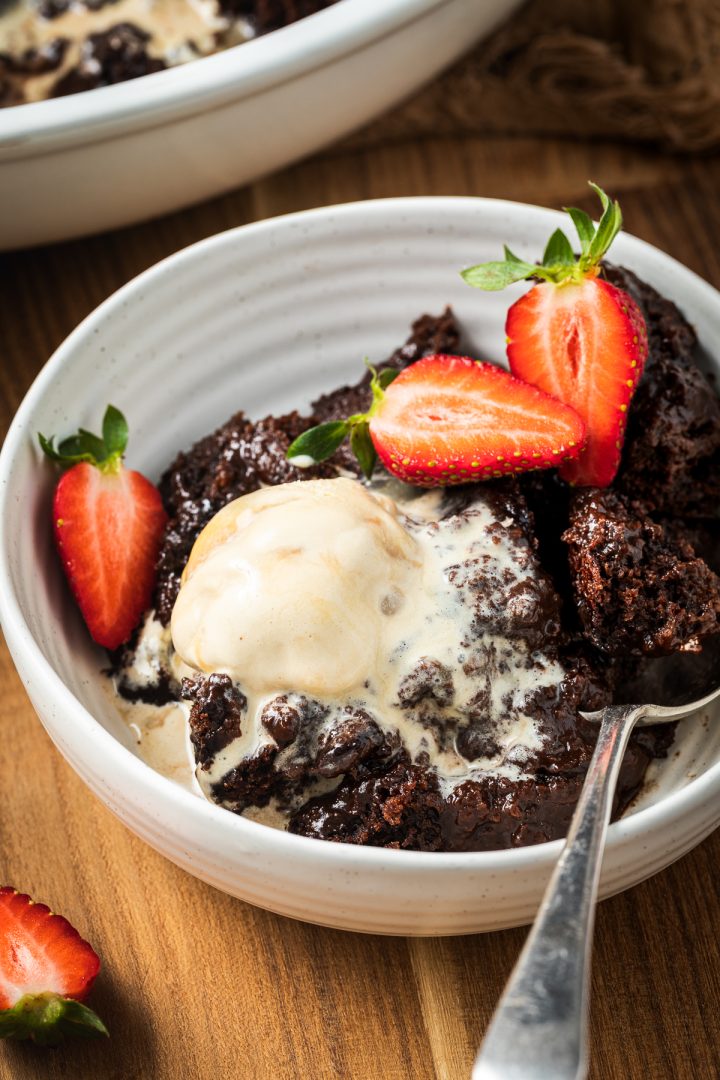 A portion of chocolate pudding in a bowl with ice cream and fresh strawberries.