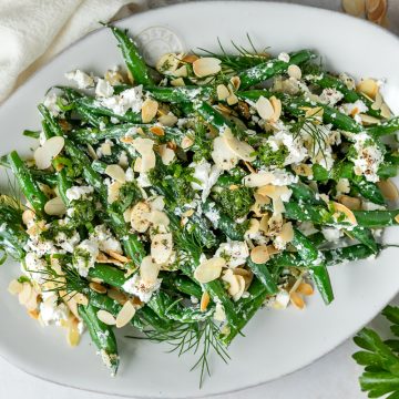 A plate of green bean salad with feta, almonds and fresh herbs.