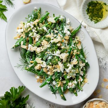 A serving plate of green beans with almonds and feta.