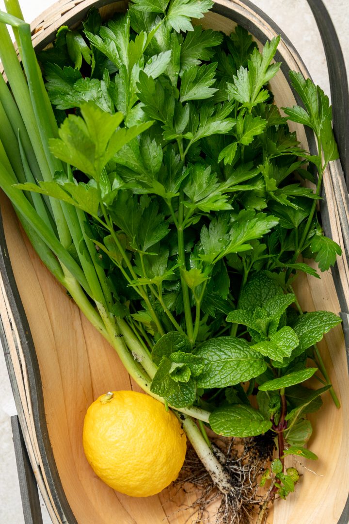 Fresh parsley, mint, spring onions and a lemon in a wooden basket.