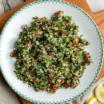 A bowl of quinoa tabbouleh surrounded by fresh lemon slices, mint and parsley.