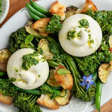 Burrata salad on a white plate topped with salsa verde and decorated with borage flowers.
