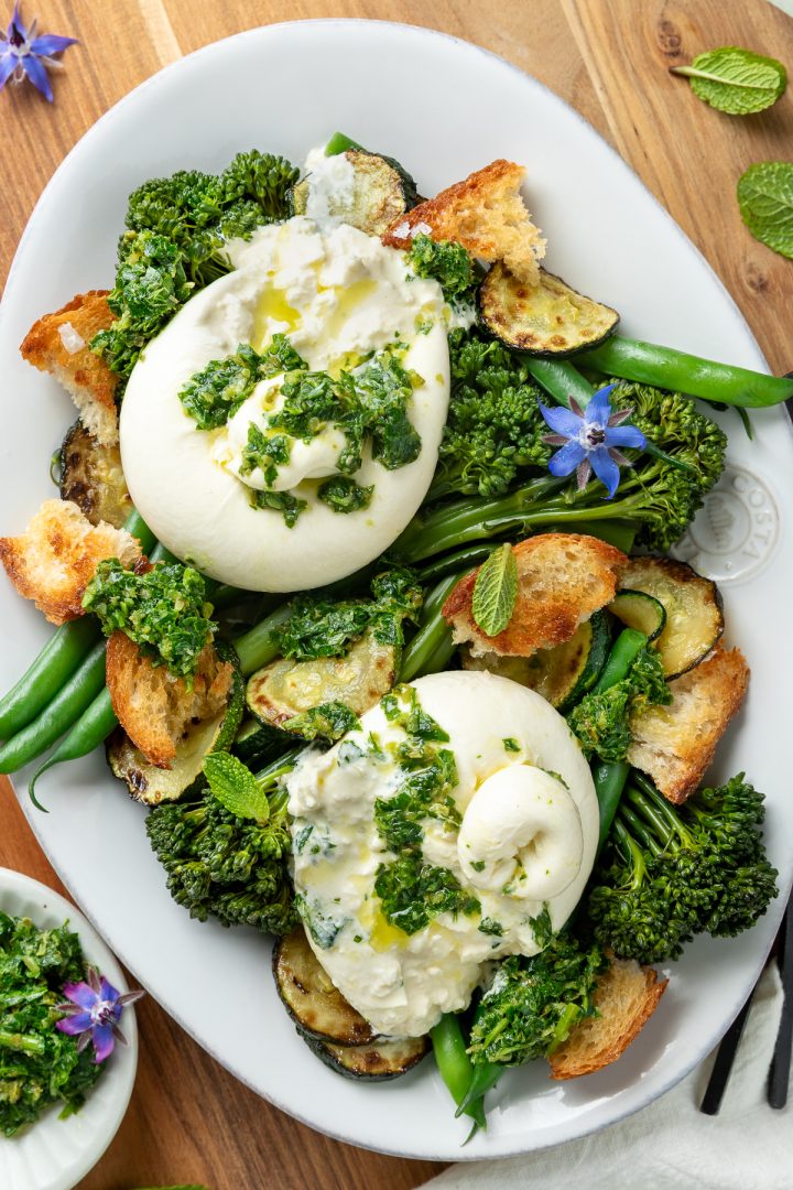 Burrata cut open on the salad, to show the creamy insides mixing with the salsa verde.