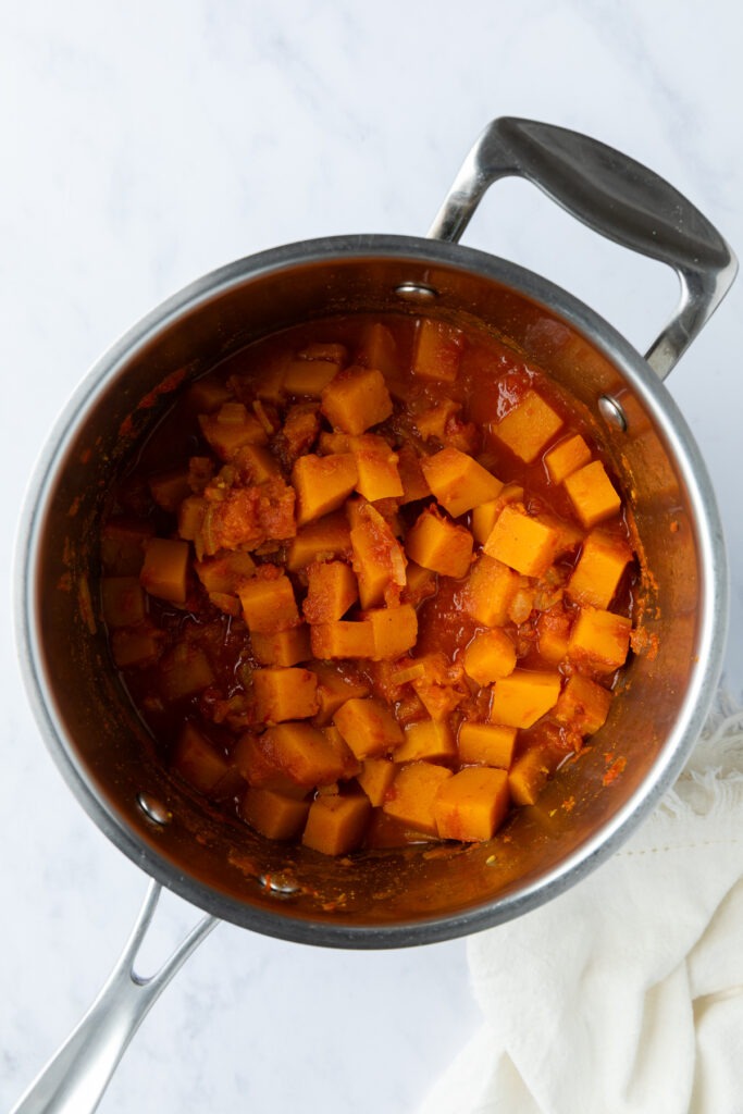 The cooked butternut squash and tomatoes in the saucepan.