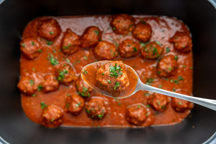 Slow cooker meatballs in a slow cooker with a spoon holding a meatball.