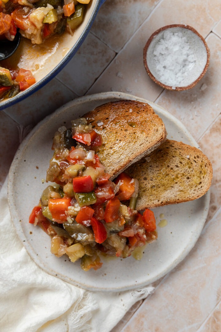 A serving of the Spanish Ratatouille on a plate with two slices of toasted bread drizzled with olive oil.