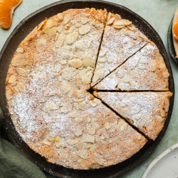 The top view of the homemade mandarin cake sprinkled with flaked almonds and topped with icing sugar.