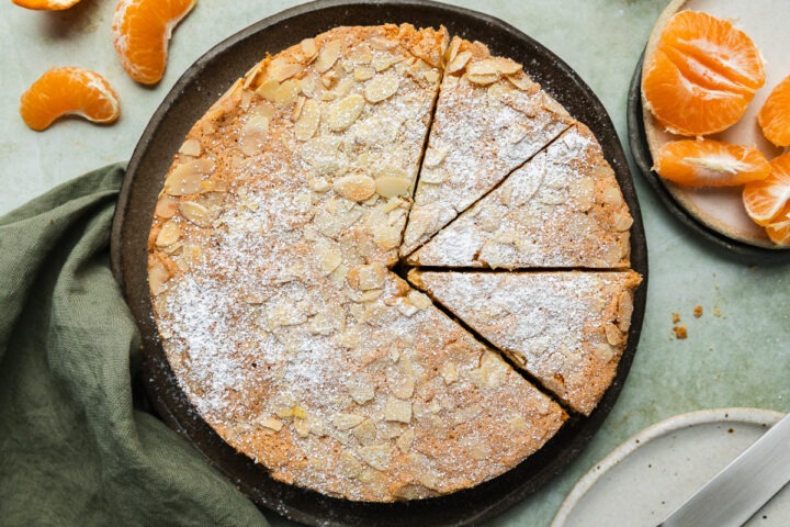 The top view of the homemade mandarin cake sprinkled with flaked almonds and topped with icing sugar.