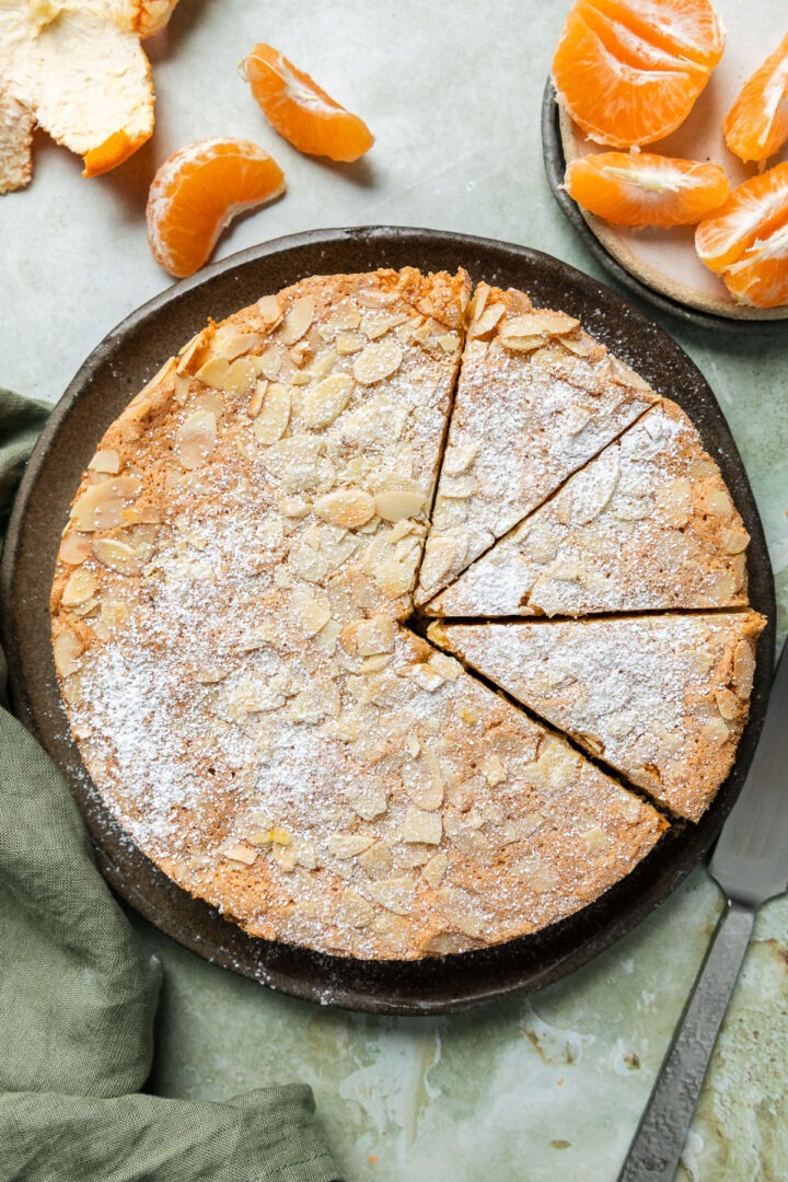 Overhead photo of the homemade mandarin almond cake to show the flaked almond top, with three slices cut out of the cake.
