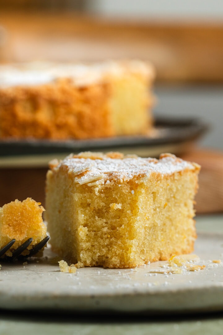 A slice of fluffy mandarin cake on a plate with a piece taken out of it.