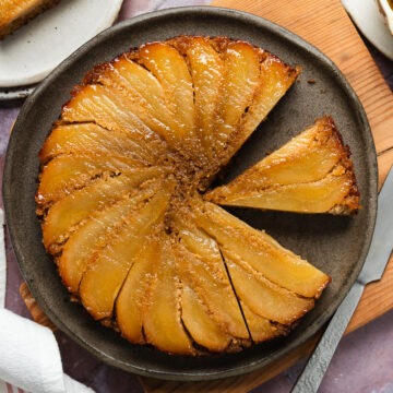 Homemade gluten-free pear upside down cake with three slices cut from it, one slice on a plate.